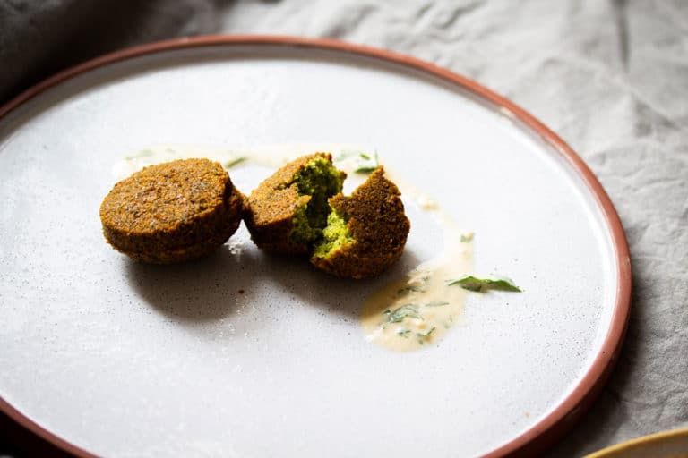 Falafel auf einem Teller. Eine Falafel ist in Mitte zerteilt und man sieht das grüne Innere.