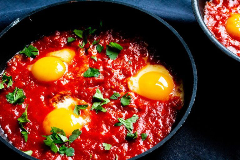 Une poêle de shakshuka est servie et est agrémentée d'un peu de coriandre.