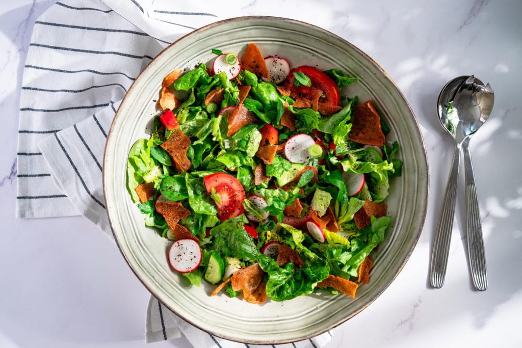 Fattoush served in a bowl. There is cutlery next to it.