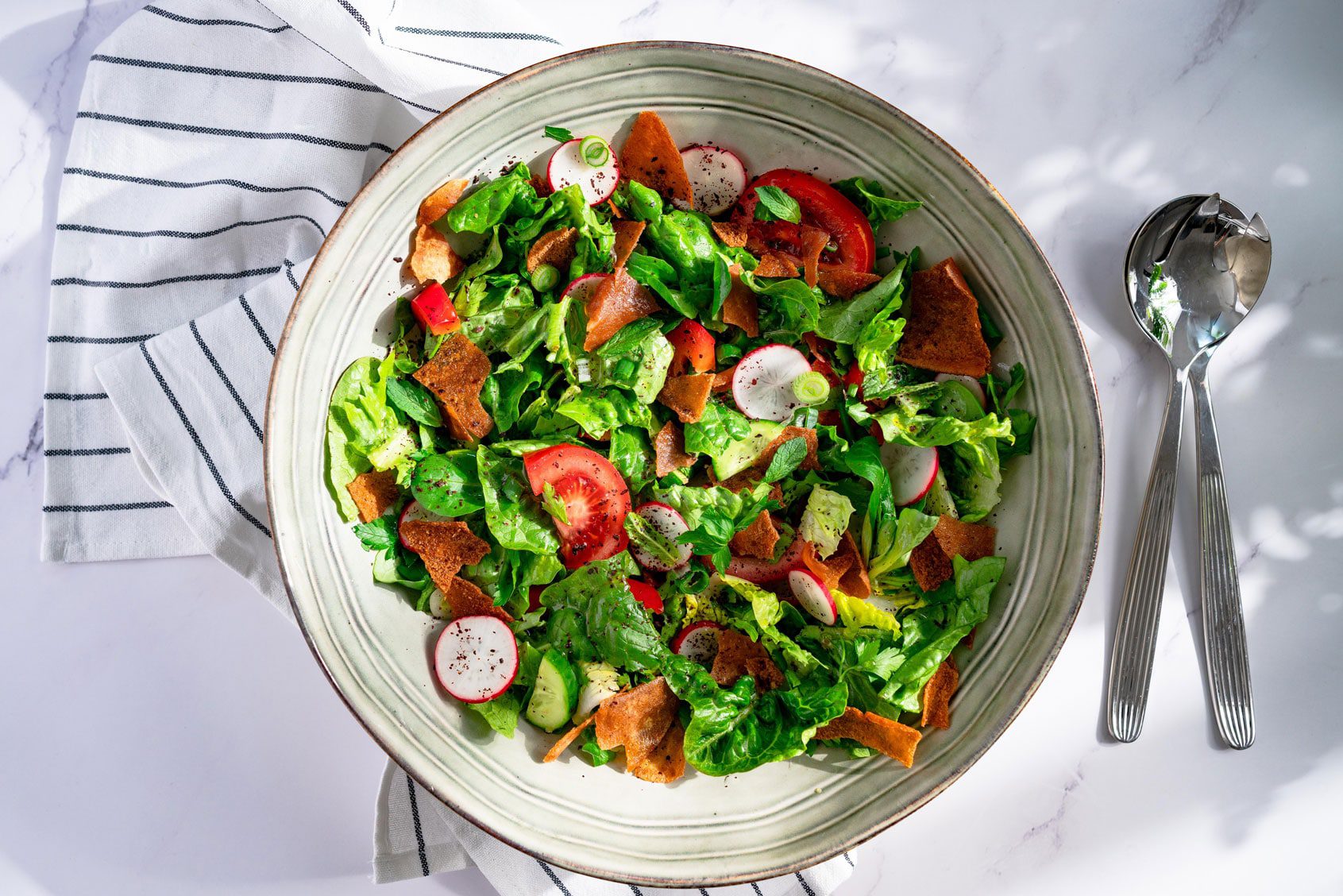 Fattoush servi dans un bol. Il y a des couverts à côté.