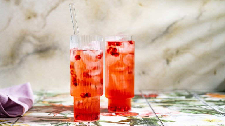 Granatapfel-Eistee mit Eiswürfeln, Granatapfelkernen und Glasstrohhalmen in zwei Gläsern serviert.