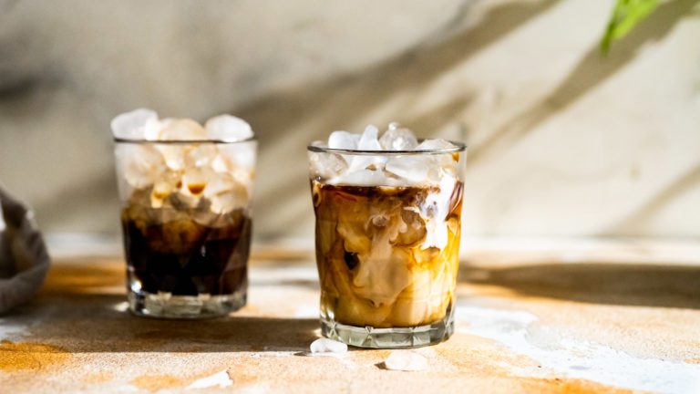 Iced mocha latte served with ice cubes in a glass. There is a second glass in the background. 