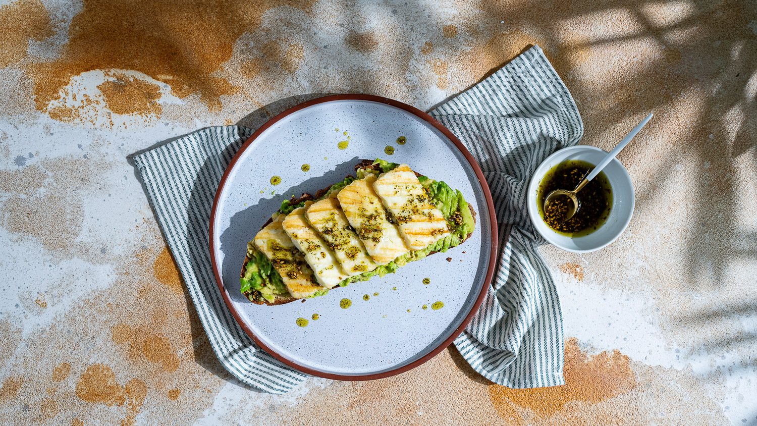 Pan de aguacate rociado con aceite de halloumi y za'atar y servido en plato.