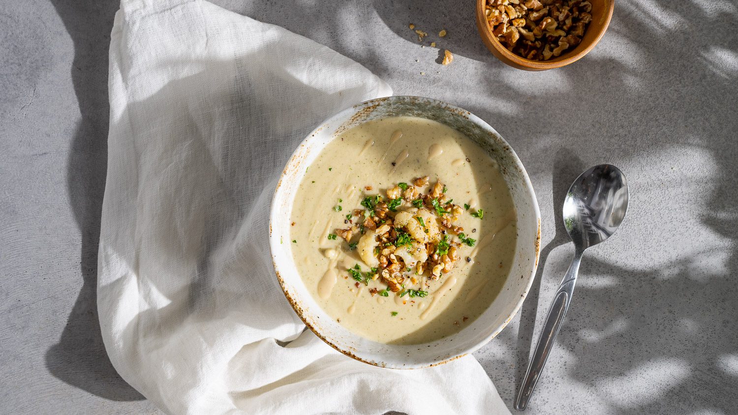 Cream of cauliflower soup with tahini, topped with walnuts and herbs, served in a bowl.