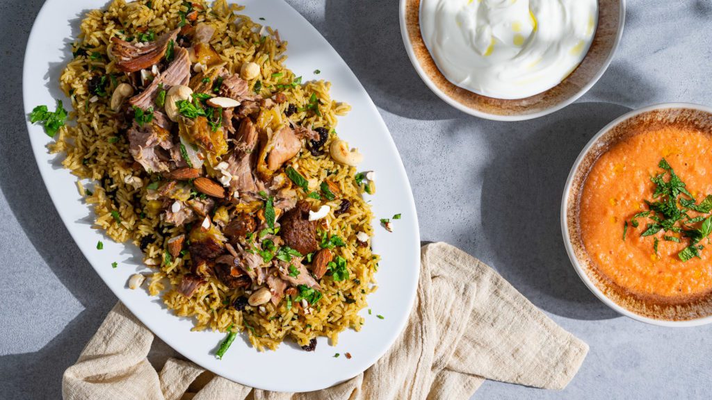 kabsa - rice with lamb served on a plate with yogurt and tomato salsa