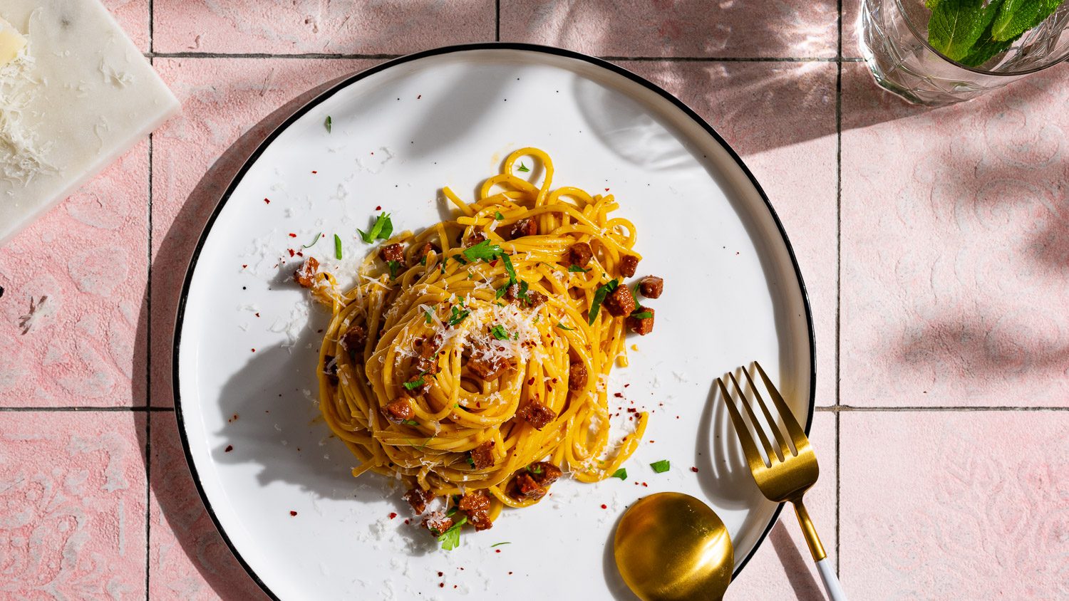 Harissa Carbonara mit Sucuk auf einem Teller serviert. Daneben liegt Besteck.