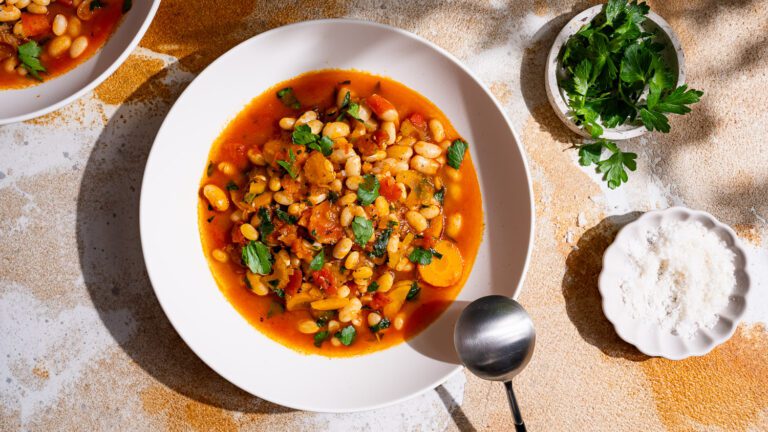 Une assiette de fasolada, deux coupelles de persil et de sel sont posées sur une table.