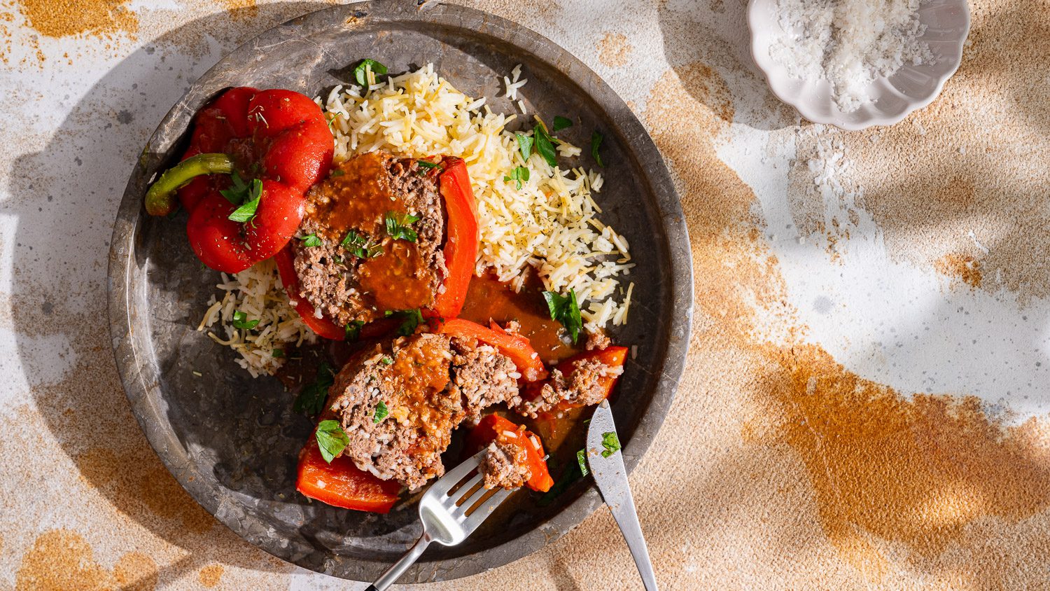 Gefüllte Paprika mit Hackfleisch liegt mit Butterreis aufgeschnitten auf einem Teller.