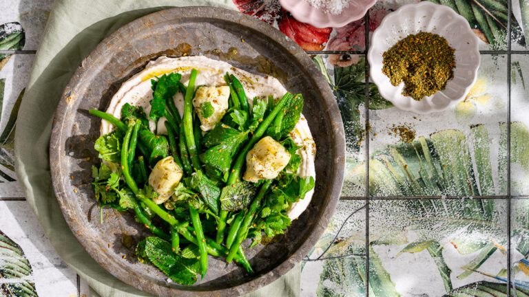 Salade de haricots verts avec artichauts et herbes sur une purée de haricots servie sur une assiette.