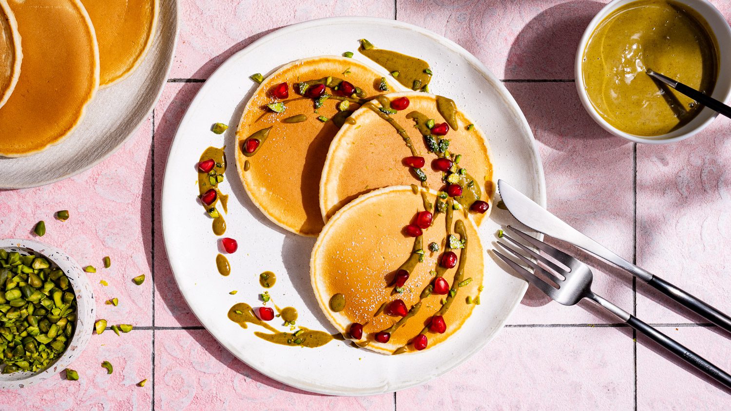 Drei Pancakes mit Pistaziencreme und Granatapfel auf einem Teller serviert.