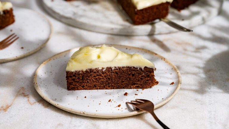 Ein Stück Gewürzkuchen mit Frosting wird auf einem Teller mit Gabel serviert.