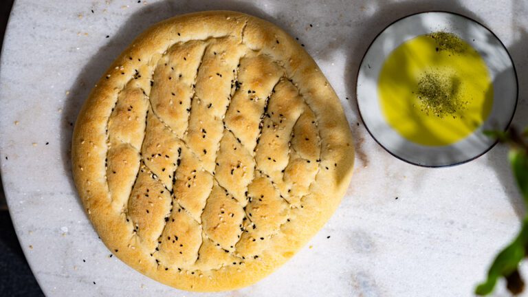 Des galettes de pain turc sont posées sur une table.
À côté se trouve un petit bol d'huile et de za'atar. 