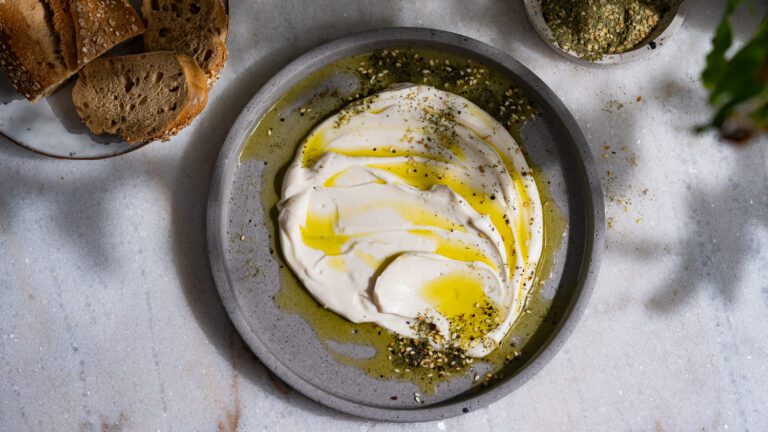 Vegnaes Labneh aus Sojajoghurt verstrichen auf einem grauen Teller. Tisch ist gedeckt mit Brot.