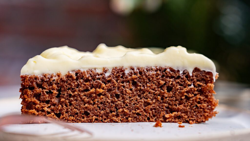 Ein Stück Gewürzkuchen mit Frischkäse-Frosting von der Seite. Man sieht, wie feinporig und saftig der Kuchen ist.