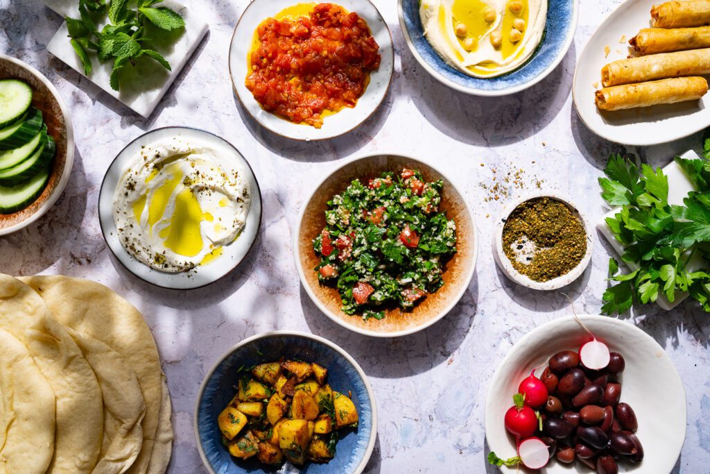 Many small bowls and plates on a light marble background as an example of a Mediterranean mezze board.