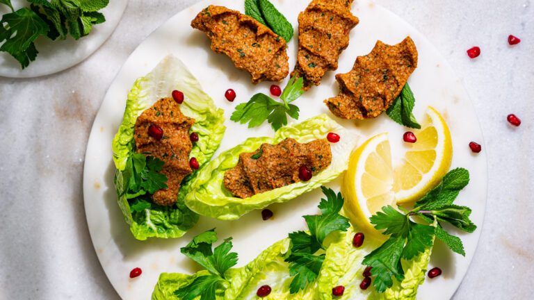 Cigköfte servi avec de la salade, des herbes, des graines de grenade et du citron.