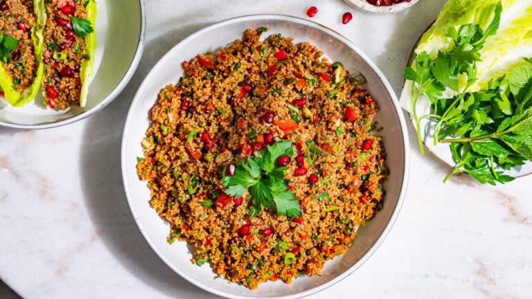 Kisir servi dans un bol. À côté, il y a des assiettes avec des feuilles de salade et des herbes aromatiques.