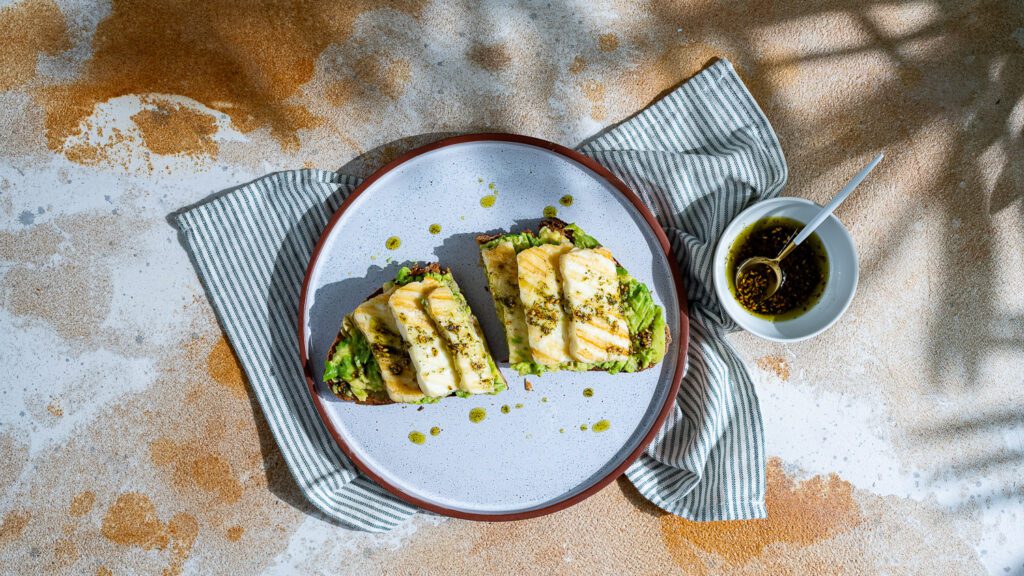 Pan de aguacate con halloumi y aceite de za'atar, cortado en rodajas y servido en plato.