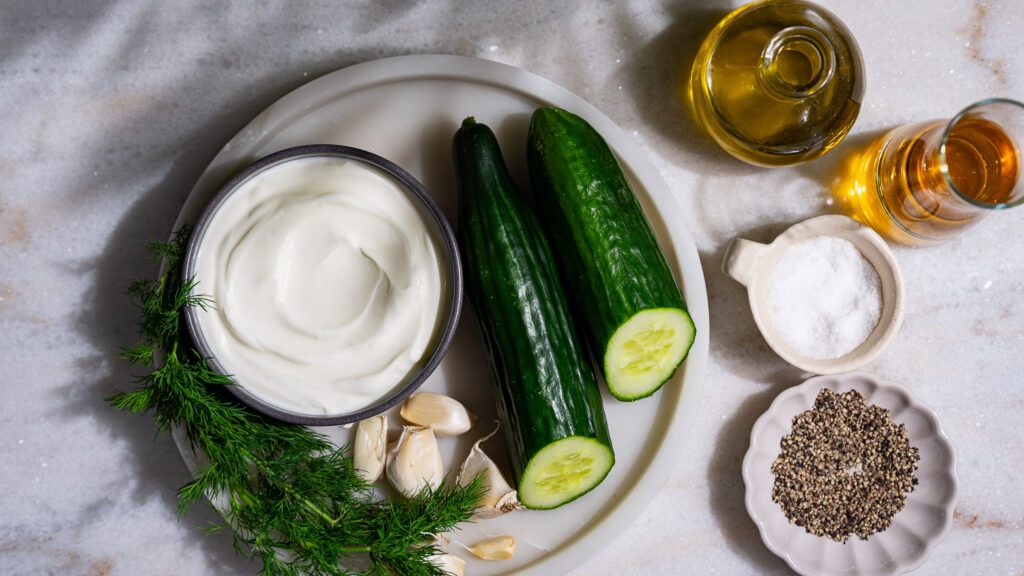 Ingredients for tzatziki are spread out on a light-colored marble base.