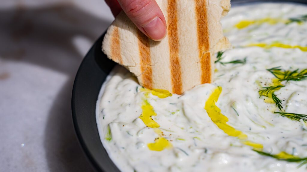 A piece of pita is dipped in tzatziki.