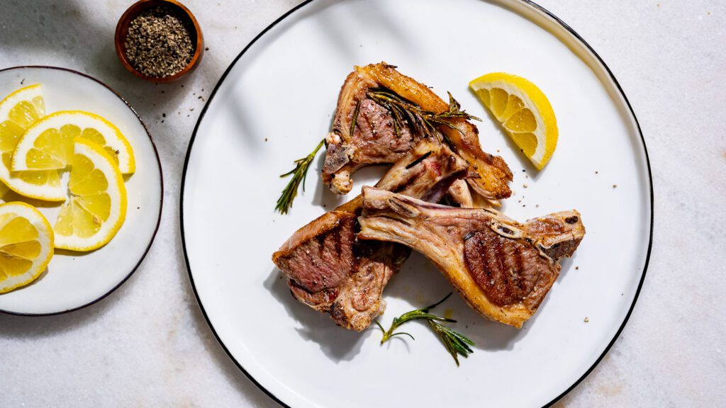 Roasted lamb chops on a plate with lemon.