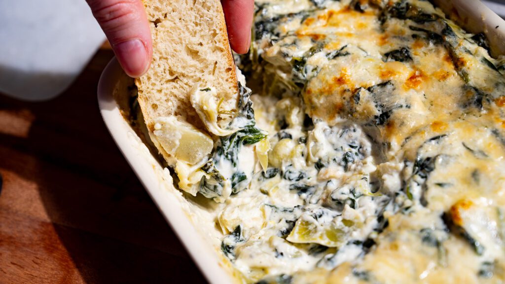 Dip a piece of baguette into the spinach and artichoke dip.