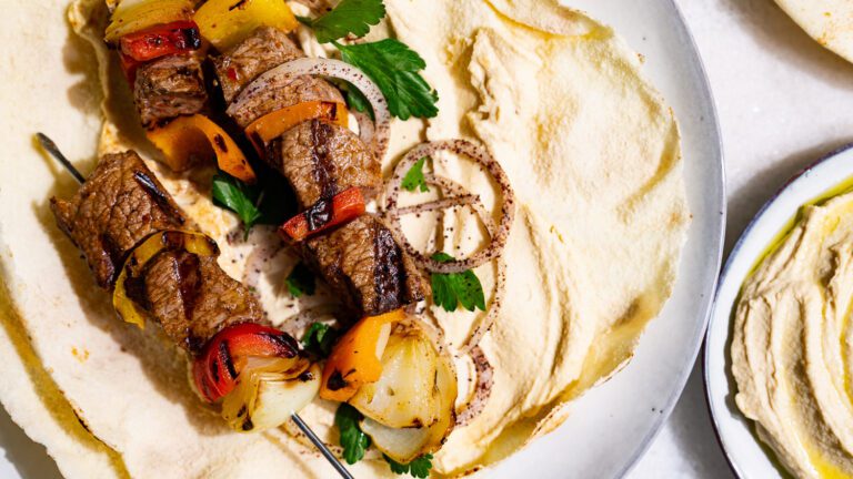 Shish kebab served on a flatbread spread with hummus.