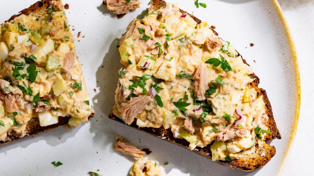 Eine Scheibe Brot mit Thunfischsalat in der Mitte durchgeschnitten auf einem Teller.