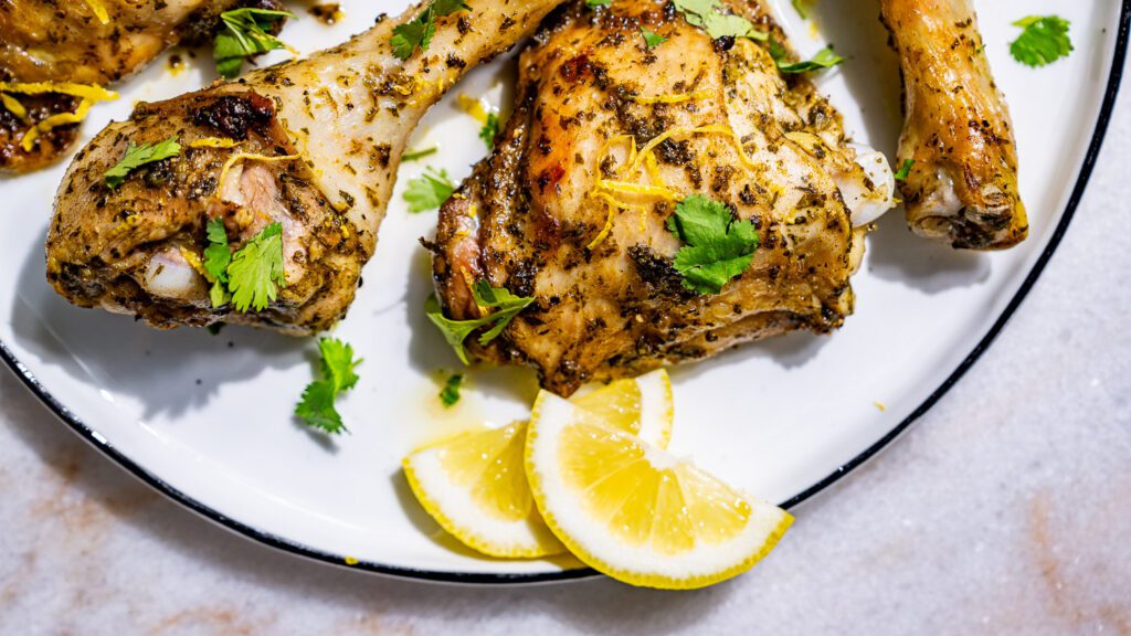 Lemon chicken served on a plate with lemon wedges and coriander.