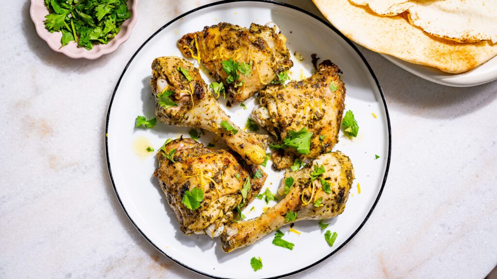 Lemon chicken served on a plate. Alongside coriander and Lebanese flatbread.