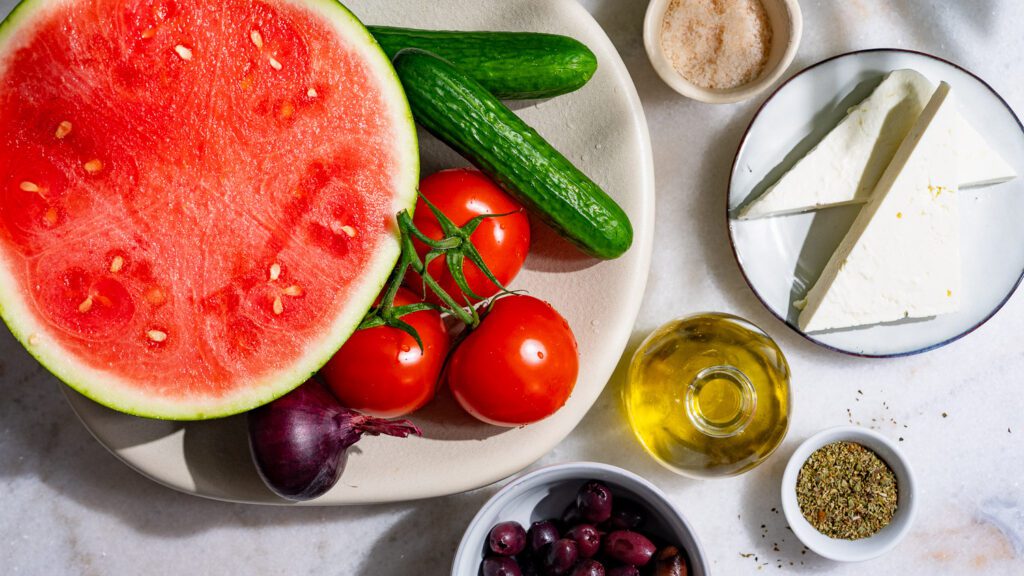 Tous les ingrédients de la salade grecque à la pastèque sont posés sur une table.