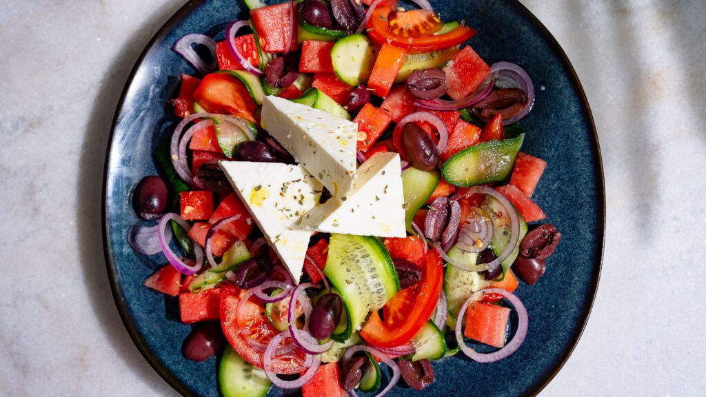 Salade grecque à la pastèque servie sur une assiette foncée.