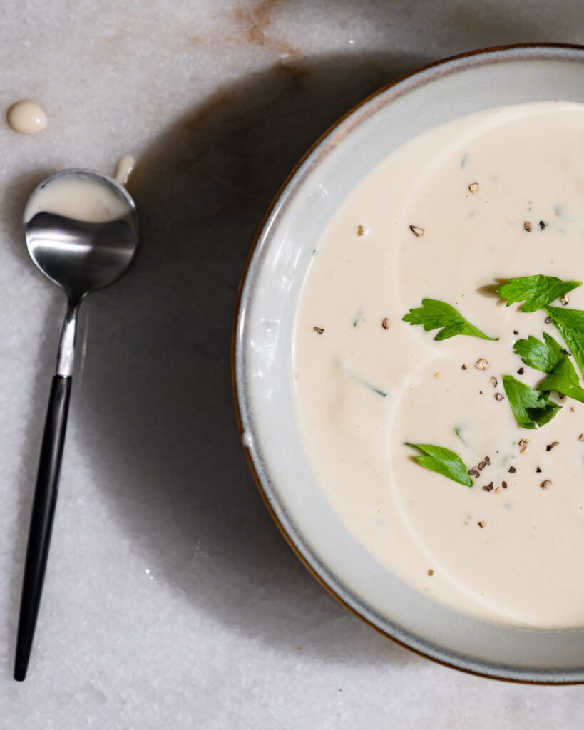 Fertige Tahini Sauce in einer Schüssel. Daneben liegt ein Löffel.