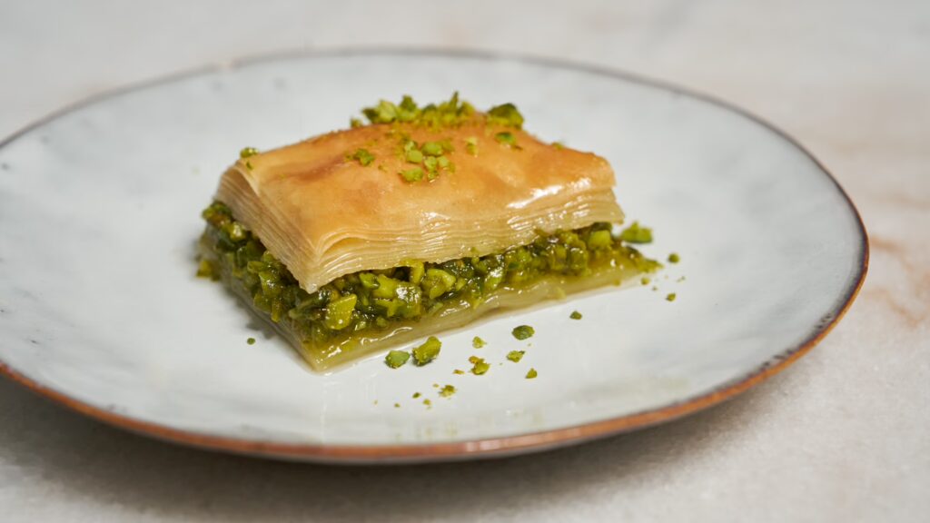 Un trozo de baklava con pistachos en un plato pequeño.