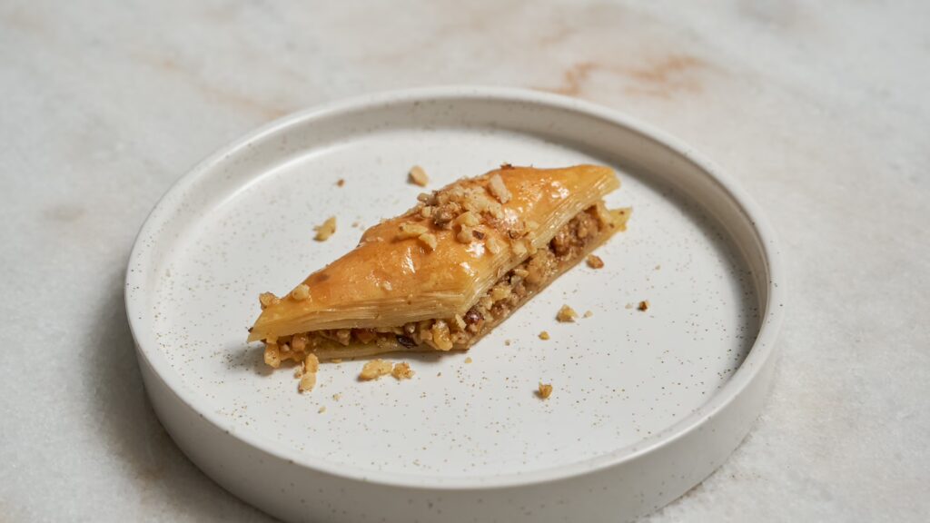 Un trozo de baklava con nueces en forma de diamante en un plato pequeño.