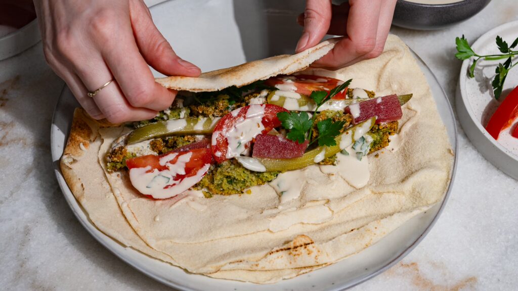 Falafel Wrap wird gerade mit zwei Händen eingerollt.