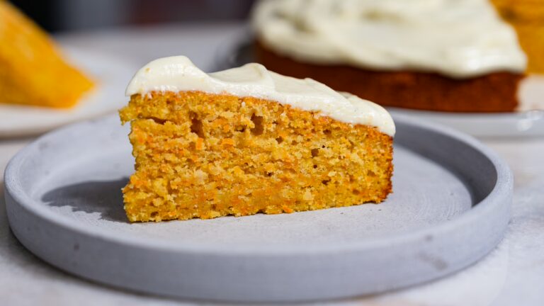 A slice of juicy carrot cake with frosting served on a plate.