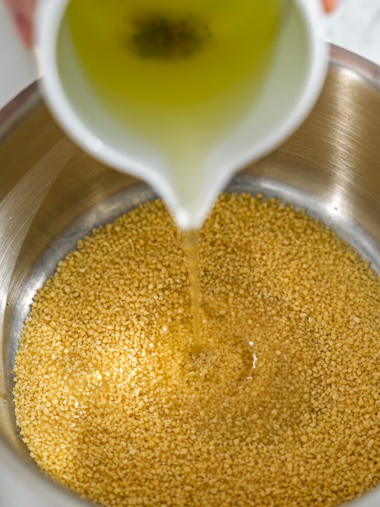 Um den Couscous zuzubereiten wird er in einem Topf mit heißer Brühe übergossen.