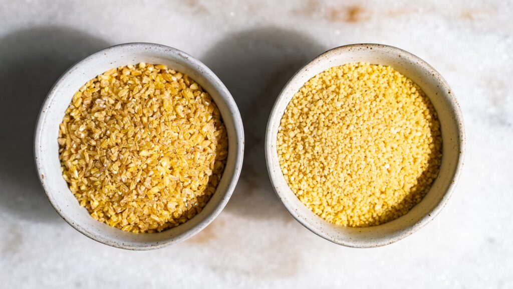Bulgur and cous cous in two small bowls next to each other to show the difference.